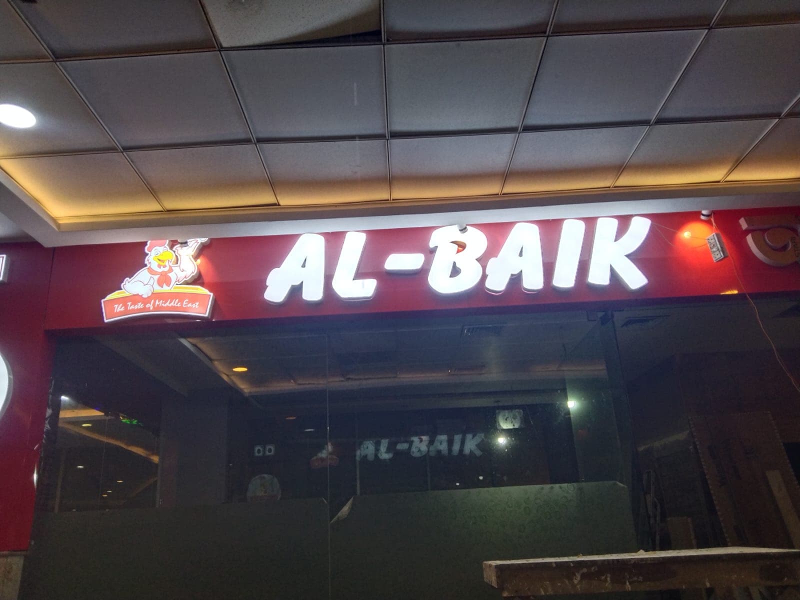 Illuminated AL-BAIK channel letters on a red restaurant facade
