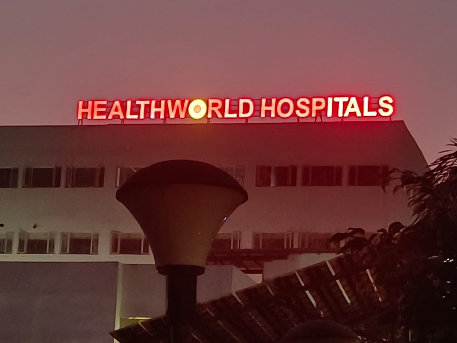 Red illuminated HEALTHWORLD HOSPITALS LED letters on a hospital building at dusk